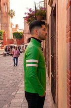 Man wearing a green jacket with reflective stripes standing on a street.
