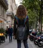 Person wearing a black leather jacket with a blue and orange backpack on a city street.